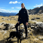 Mann steht mit Hund an der Leine in einer Berglandschaft